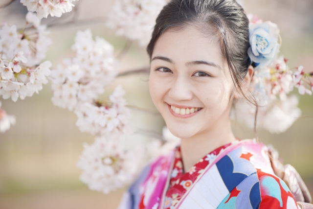 桜の木の前で振袖を着て微笑む女性